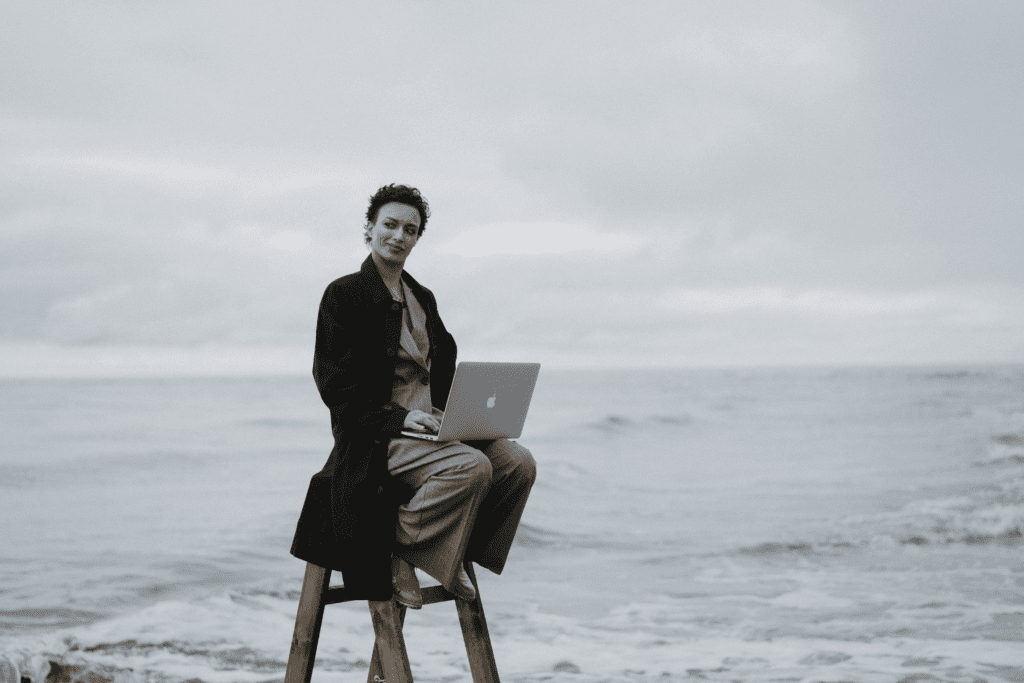 Woman sitting on stool by the ocean working on her laptop
