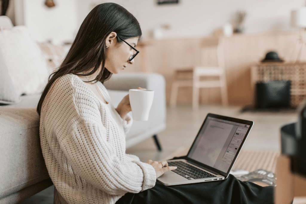 Young female solopreneur sitting with her laptop and a cup of coffee.
