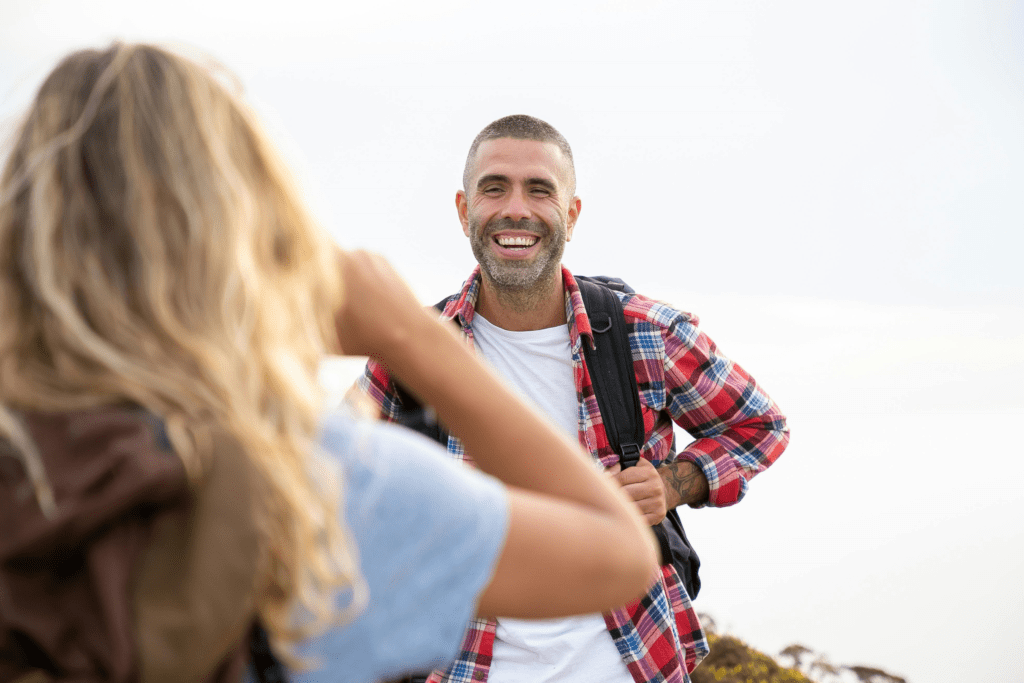 A male backpacker smiling and a woman taking his photo