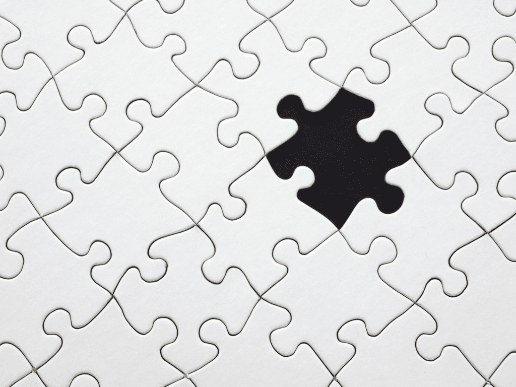 A jigsaw puzzle with all white pieces that has a black space for one missing piece.