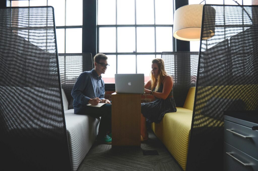 Male and female sitting in a joint workspace reviewing a document on a laptop.